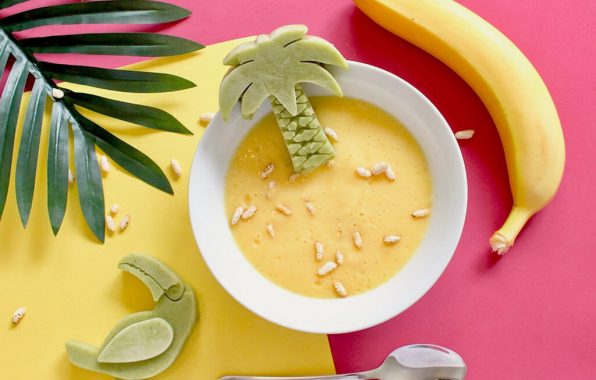 Koolhydraatarme vanillepudding in een glas, gegarneerd met fruit, op een roze achtergrond met banaan en palmbladeren
