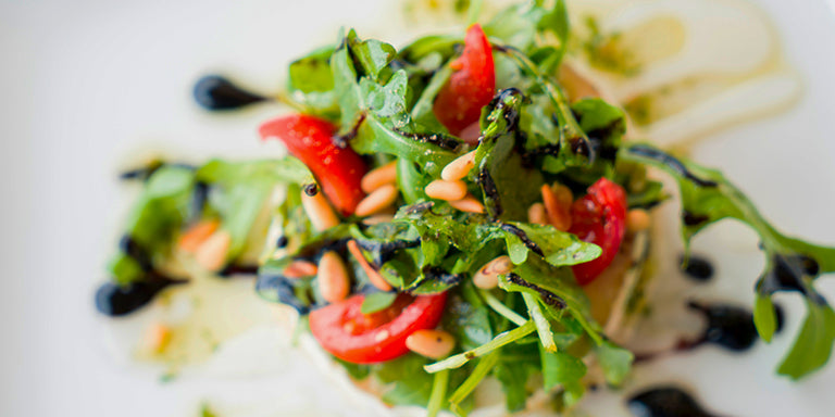 Tonijnsalade met rucola, cherrytomaatjes en geroosterde pijnboompitten op een wit bord — koolhydraatarm keto lunchrecept