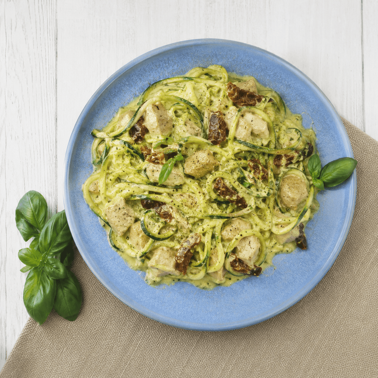Romige kip met courgette noedels in kokosmelksaus met zongedroogde tomaat en verse basilicum in een blauw bord — koolhydraatarm dinerrecept