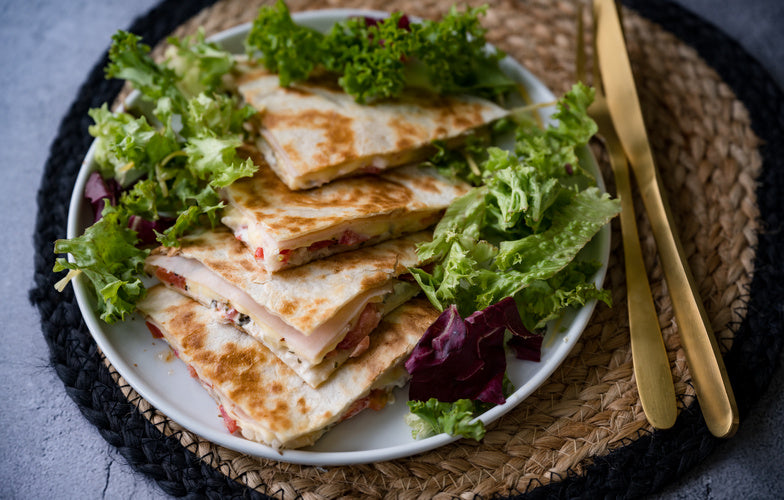 Goudbruine chicken quesadilla's in driehoeken gesneden op een bord met gemengde sla en tomaat