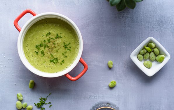 Romige groene tuinbonensoep in een rode soeppan met verse peterselie en tuinbonen als garnering