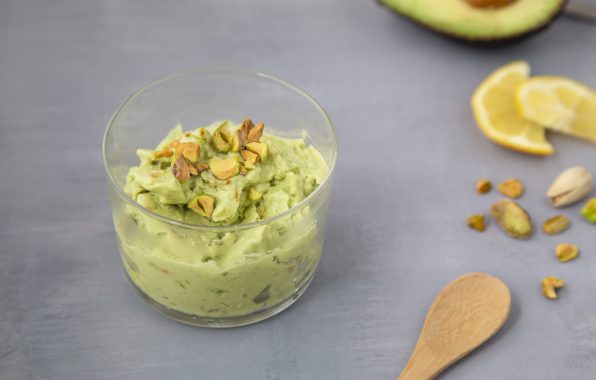 Koolhydraatarm avocado-ijs met fijngehakte pistachenoten en een schijfje citroen, geserveerd in een klein bakje op een houten lepel