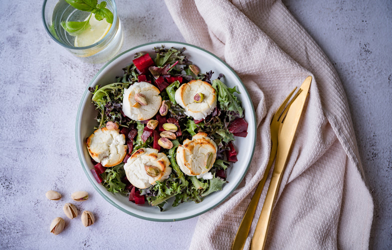 Bietensalade met warme gegrilde geitenkaas, rode biet, pistachenoten en honingbalsamicodressing in een saladeschaal