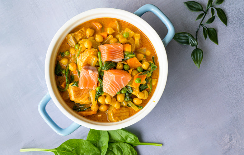 Gele curry met zalm, spinazie en kikkererwten in een blauwe pan met verse koriander