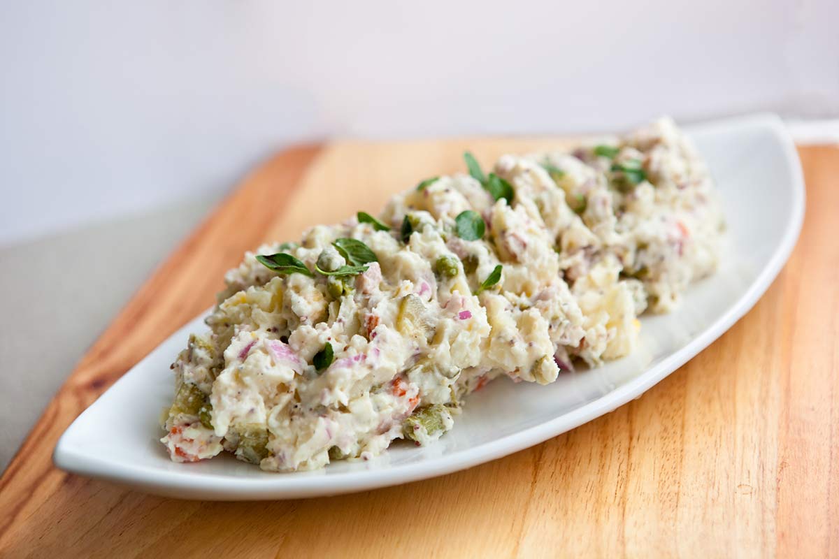 Koolhydraatarme huzarensalade met bloemkool, corned beef, augurk en kappertjes op een wit bord — koolhydraatarm recept van Makkelijk Afvallen
