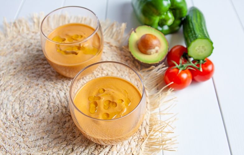 Spaanse gazpacho in twee glazen met tomaten, komkommer, avocado en paprika op de achtergrond