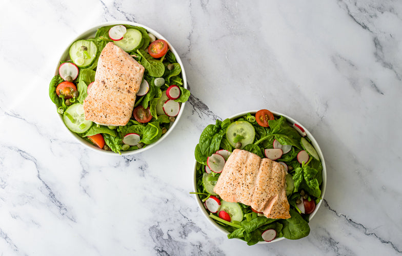 Salade van zalm en komkommer met spinazie, radijs, cherrytomaatjes en kappertjes in een diep bord
